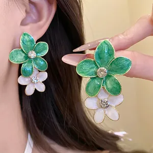 Macro view of green and white floral enamel earrings with sparkling rhinestone centers.