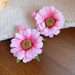 Detailed view of pink fabric flower earrings with raffia balls and silver pins.