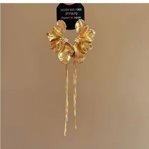 Macro detail of elegant gold flower earrings with long, delicate shimmering tassels