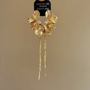 Close-up of elegant gold flower earrings with long delicate tassels and metallic texture