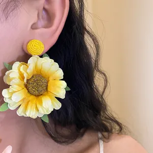 Detail view of yellow sunflower fabric earrings with raffia studs on a model.