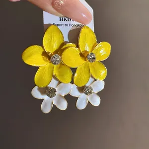 Close-up view of yellow and white enamel flower stud earrings with sparkling center rhinestones