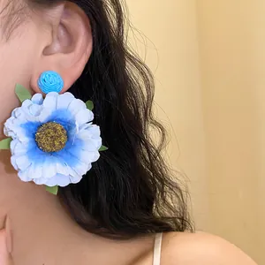 Detailed view of oversized light blue fabric flower earrings with raffia stud on model
