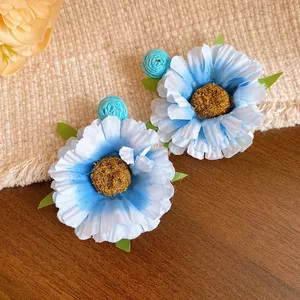 Detailed shot of blue raffia fabric flower earrings with silver needles on wooden background