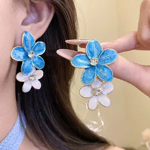 Close-up detail of blue and white enamel flower earrings with rhinestone centers.