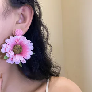 Macro detail of elegant pink raffia fabric flower drop earrings worn by a model.
