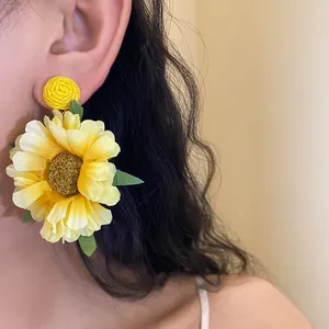 Close-up of large yellow fabric sunflower earrings with raffia stud and green leaf details.