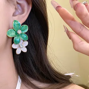 Detailed view of green and white enamel flower earrings with sparkling rhinestone center.