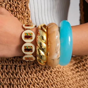 Détail en gros plan montrant des bracelets en émail, métal doré et résine bleue au poignet.