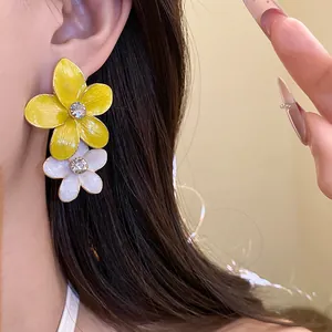 Macro view of yellow and white enamel floral earrings with sparkling rhinestone centers.