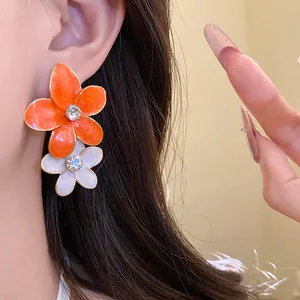 Close-up of orange and white drip oil flower earrings featuring sparkling rhinestones