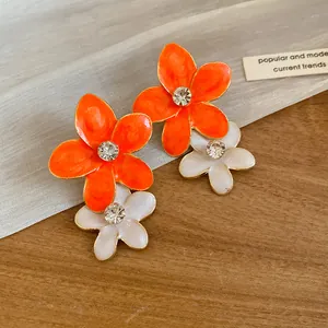 Close-up of vibrant orange and white enamel flower earrings with sparkling rhinestones