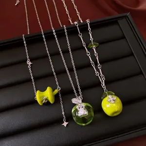 Close-up of green apple and bear pendant necklaces on a black jewelry tray.