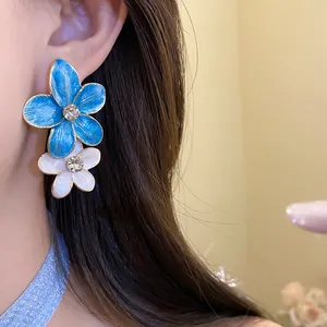Detail shot of blue and white enamel flower earrings with sparkling rhinestone centers.