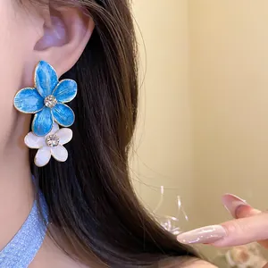 Close-up of elegant blue and white enamel flower drop earrings with sparkling rhinestones
