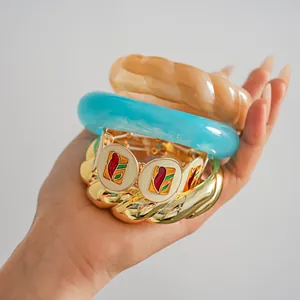 Détail de bracelets empilés en résine colorée et bracelets en émail doré tenus en main