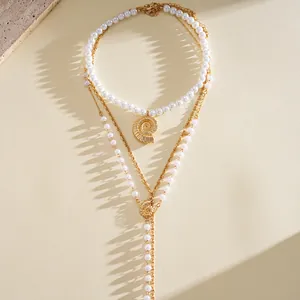 Detail view of a three-layered gold chain necklace with pearls and golden seashell pendants