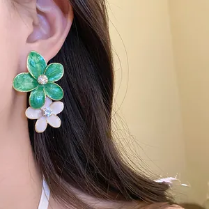 Close-up detail of floral drop earrings with green and white petals and sparkling rhinestones