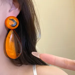 Detaillierte Makroansicht von großen orangefarbenen Harz-Ohrringen im Retro-Stil
