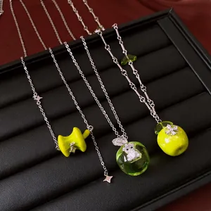 Close-up of green apple pendants with rhinestone star and bear details on silver chains