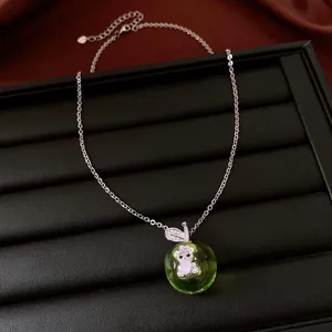 Close-up detail of a green apple pendant necklace featuring a sparkling bear design.