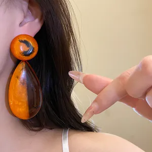 Nahaufnahme von orangefarbenen Bernstein-Resin-Ohrhängern im Vintage-Stil getragen von einem Model