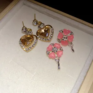 Primo piano di orecchini a cuore d'ambra e fiori rosa in una scatola regalo.