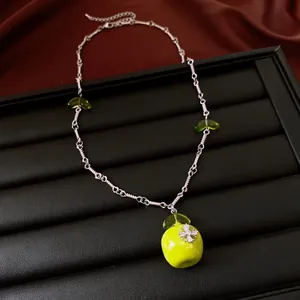 Detail view of a silver necklace with a green apple pendant and star decoration