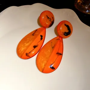 Nahaufnahme der orangefarbenen Vintage-Harzohrringe mit Tintenmuster auf weißem Teller.