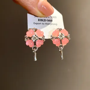 Dettaglio ravvicinato di eleganti orecchini a fiore con petali a cuore rosa e strass lucidi.