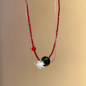 Dettaglio collana in cristallo rosso con perla nera e ciondolo a forma di fiore chiaro