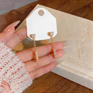 Close-up detail of gold-plated tassel earrings featuring sparkling zircon studs and bar.