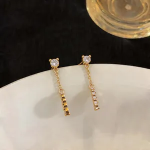 Close-up of minimalist gold drop earrings with zircon stones and vertical bar tassel.