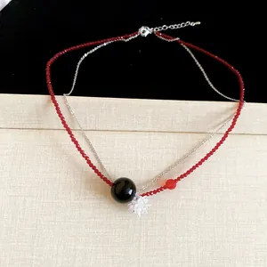 Primo piano dell'elegante collana a due strati con perline rosse e ciondolo a fiore.