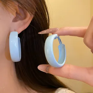 Close-up of minimalist light blue spray-painted hoop earrings being worn and held