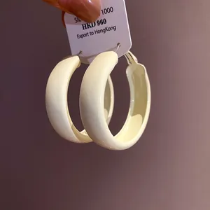 Close-up of minimalist cream-colored hoop earrings with silver needle detail