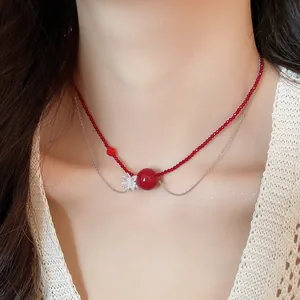 Dettaglio di una collana a due strati con perle di cristallo rosse e un ciondolo a fiore.