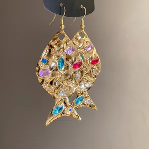 Close-up of gold fish earrings with colorful crystals and wrinkled texture.