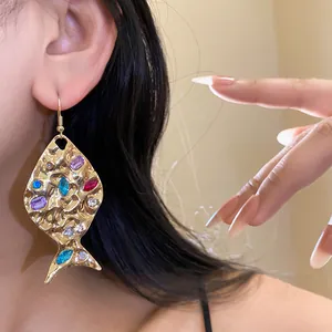 Close-up of vintage gold fish drop earrings featuring colorful rhinestones on model's ear