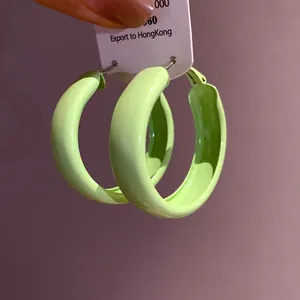 Close-up detail of vibrant lime green spray-painted hoop earrings with hypoallergenic silver needles