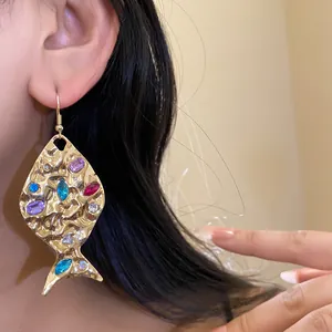 Detail view of a golden wrinkled fish earring with colorful rhinestones on a model.