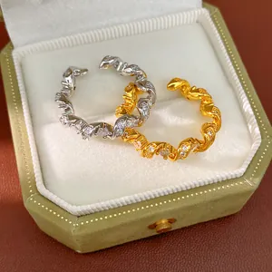 Détail rapproché de bagues torsadées en argent et or avec zircons dans un écrin vert