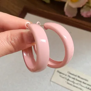 Close-up of pink spray-painted minimalist hoop earrings with silver needles held by hand