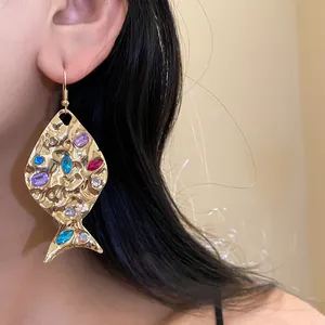 Close-up detail of gold fish-shaped earring with colorful rhinestones worn by a model.