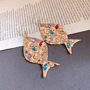 Detail view of vintage gold fish earrings with colorful rhinestones and hammered texture.