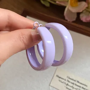 Close-up of glossy lavender purple hoop earrings held by hand against a warm background.