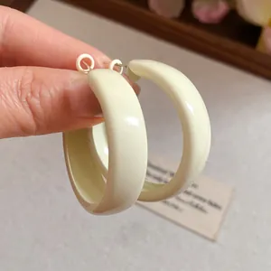 Cream-colored painted hoop earrings in dopamine style shown in a detailed hand-held view