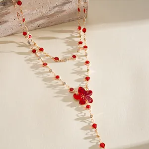 Close-up detail of a gold-tone necklace featuring vibrant red resin flowers and gems.