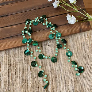 Dettaglio di una collana bohémien con perline di conchiglia verdi e catena dorata