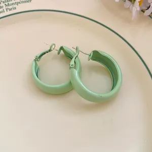 Close-up of light green spray-painted hoop earrings on a vintage cream ceramic plate